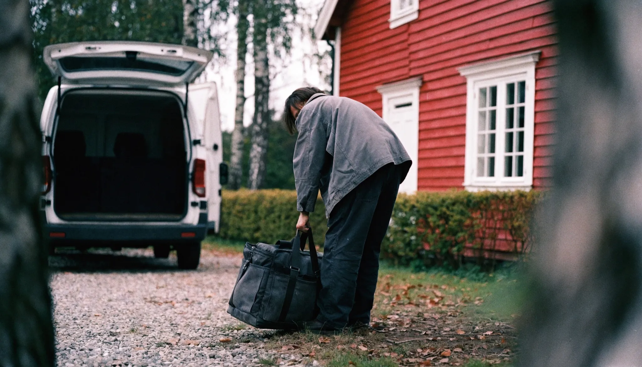 Rörmokare som lyfter en verktygsväska ur en servicebil utanför ett rött trähus